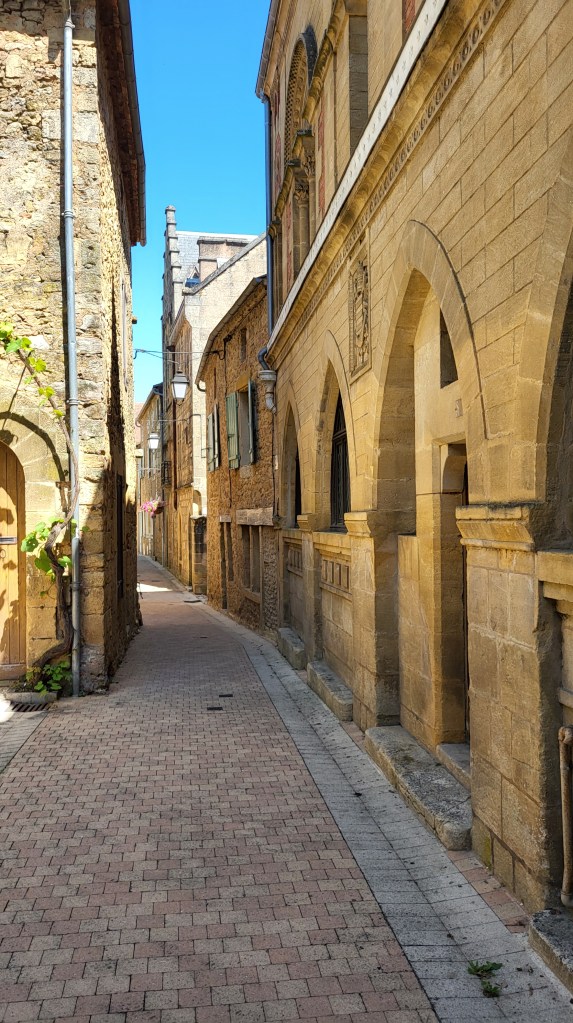 Empty cobbled lane in Belvès framed by historic stone buildings on a summer afternoon